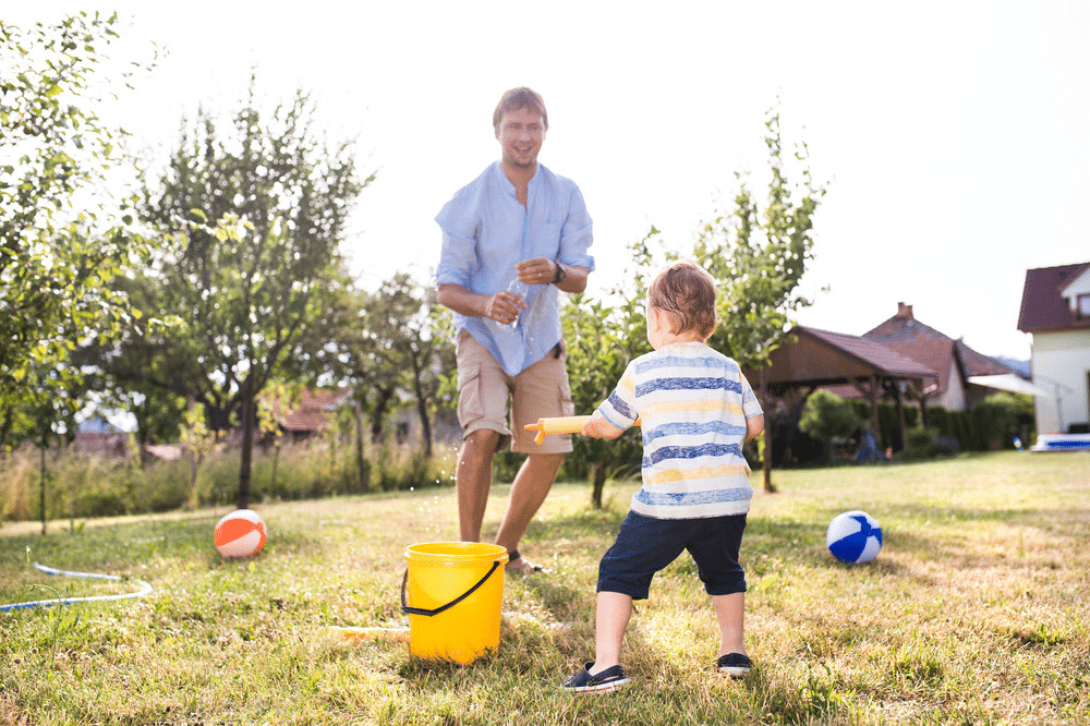 image Father and child playing with water and beach balls in sunny backyard, enjoying summer fun together. | Sky Rye Design Father and child playing with water and beach balls in sunny backyard, enjoying summer fun together.