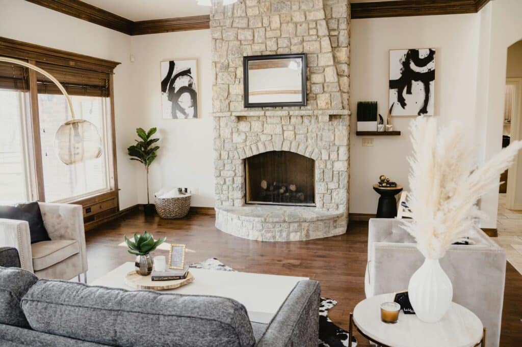 image Modern living room with stone fireplace, abstract art, cozy seating, and plants, showcasing elegant decor and natural light. | Sky Rye Design Modern living room with stone fireplace, abstract art, cozy seating, and plants, showcasing elegant decor and natural light.
