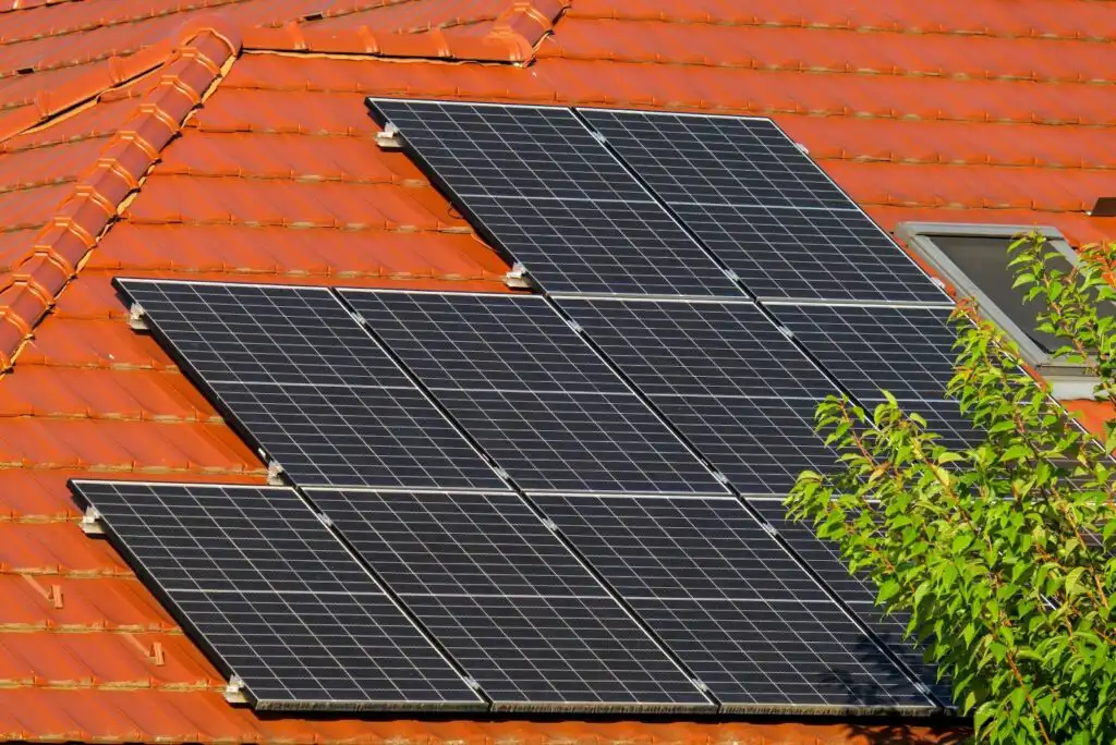 Solar panels on a red tiled roof, capturing sunlight for eco-friendly energy, with a leafy tree in the foreground.