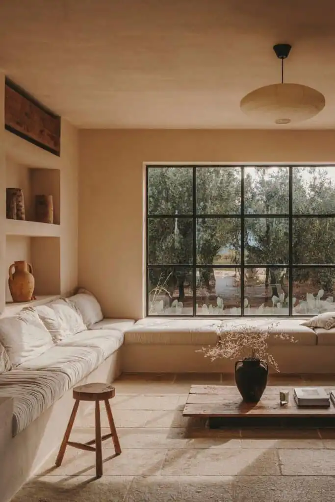 Cozy minimalist living room with large window, rustic wooden coffee table, and built-in seating. Neutral tones and natural
