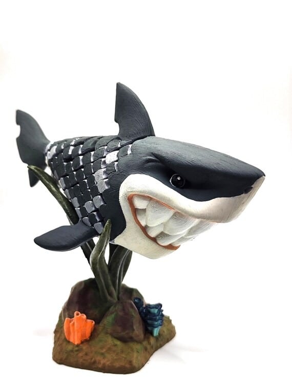 Smiling shark figurine with exaggerated teeth, set on a decorative base with coral, showcasing a playful aquatic theme.
