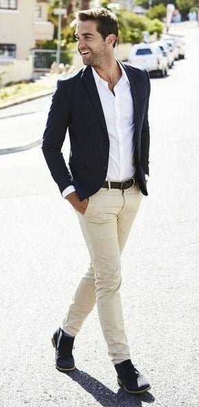 Man walking confidently on a sunny street, dressed in a navy blazer, white shirt, beige pants, and black shoes. Casual