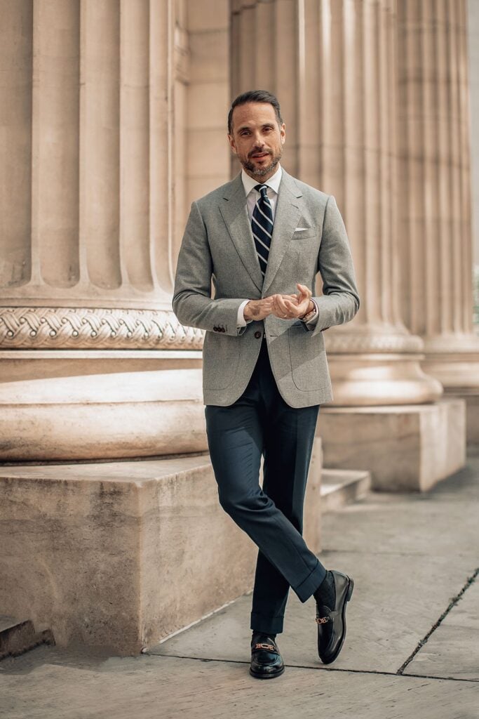 Man in stylish gray suit and striped tie stands confidently by elegant columns, exuding sophistication and professionalism.