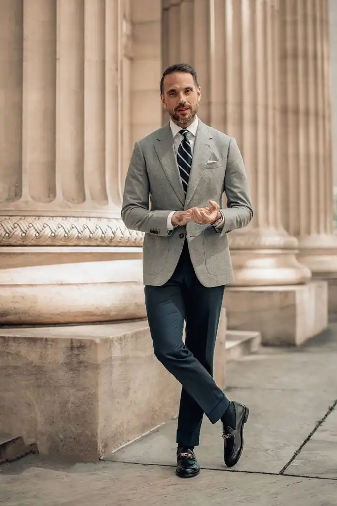 Man in stylish gray suit and striped tie stands confidently by elegant columns, exuding sophistication and professionalism.
