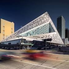 Unique triangular building with modern design in urban setting, featuring dynamic street view and blurred motion of passing