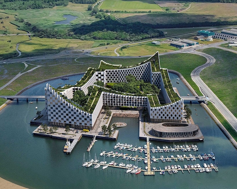 Aerial view of innovative waterfront building with green roofs and integrated marina, surrounded by lush landscape and rural