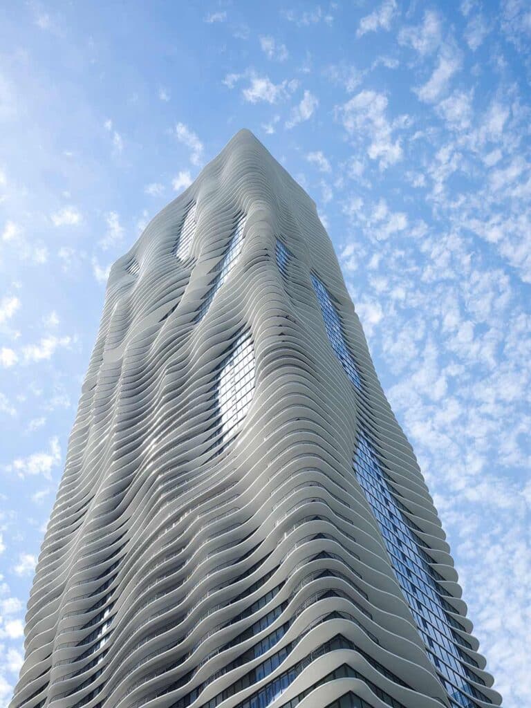 Modern skyscraper with wavy facade against a cloudy blue sky, showcasing innovative architectural design and urban skyline