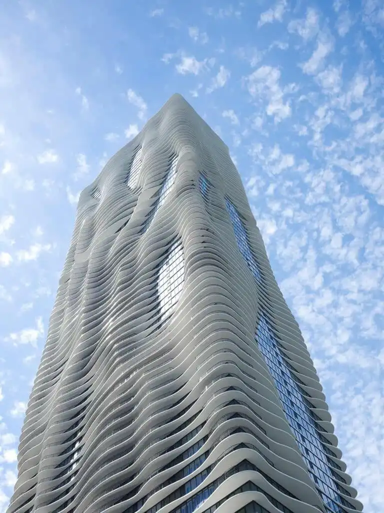 Modern skyscraper with wavy facade against a cloudy blue sky, showcasing innovative architectural design and urban skyline