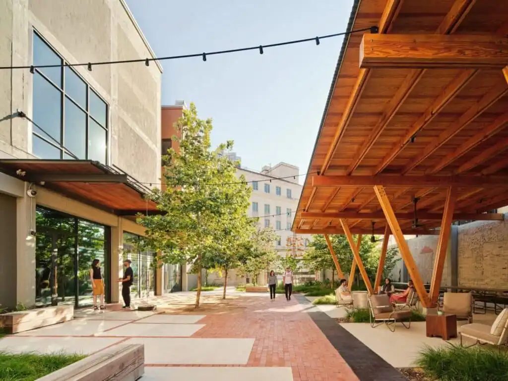 Modern outdoor seating area with wooden pergola, urban landscaping, and people enjoying a sunny day in a contemporary