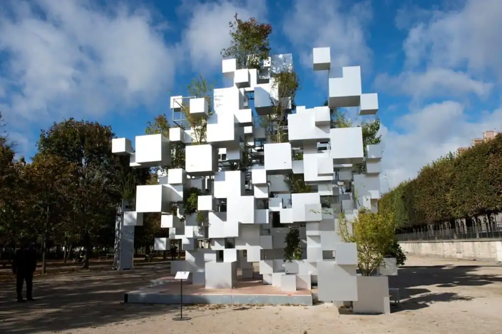 Modern outdoor art installation of white cubic structures with integrated greenery under a vibrant blue sky.