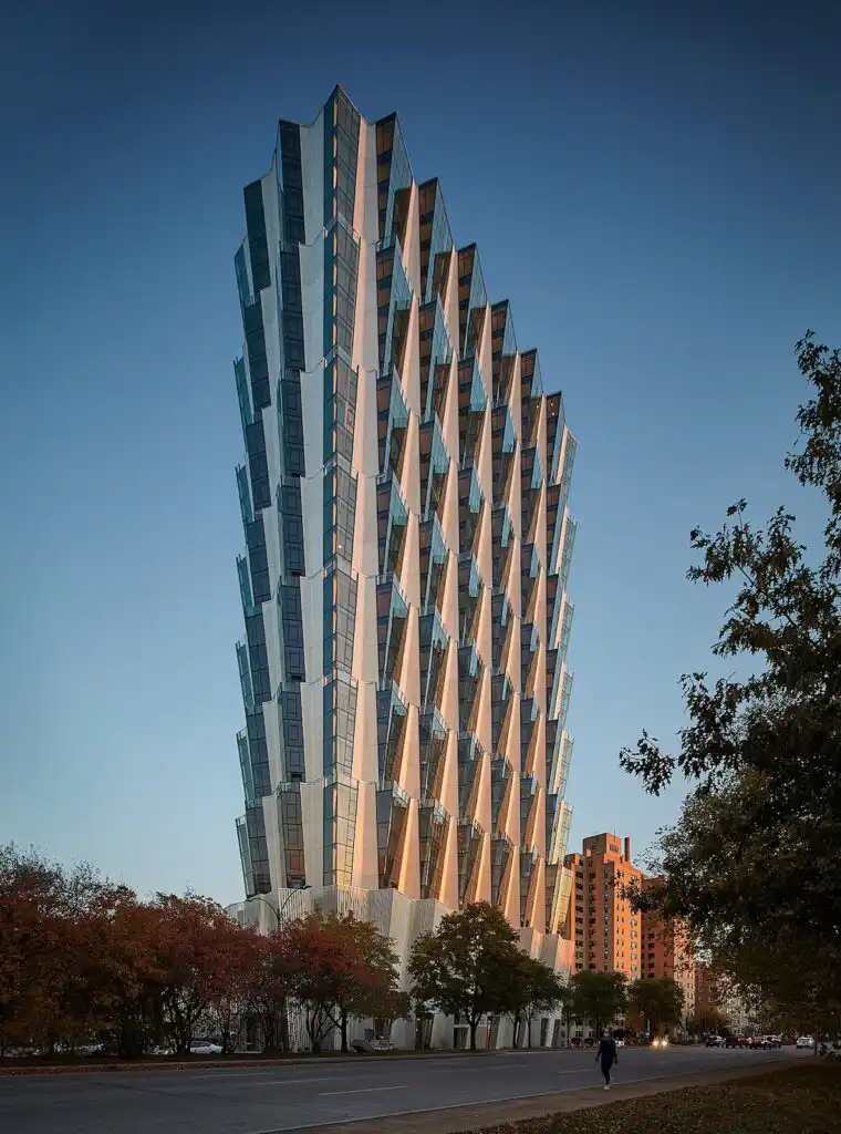 Striking modern high-rise with geometric glass facade, set against a clear sky, lined with autumn trees on an urban street.