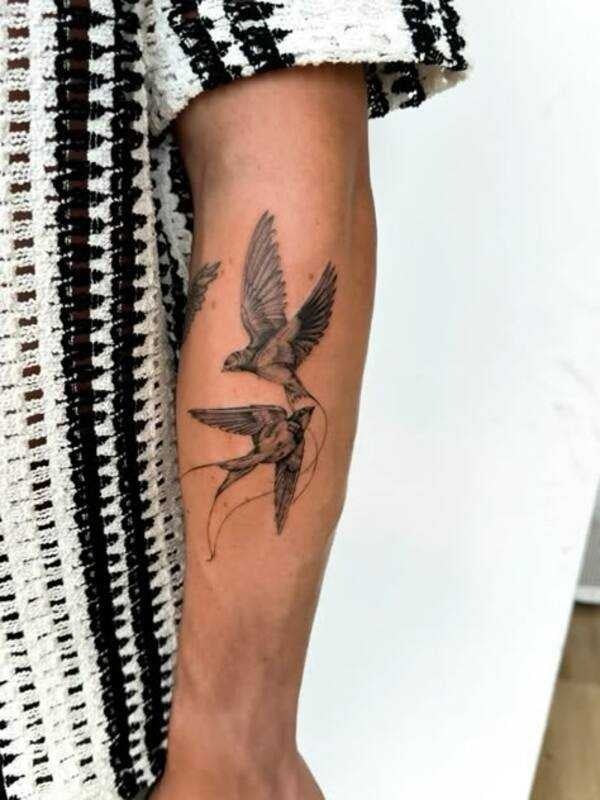 Arm tattoo showcasing two intricately designed birds in flight, set against a textured black-and-white knitted fabric