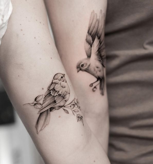 Matching bird tattoos on two people's arms, featuring a perched bird and a flying bird, symbolizing connection and freedom.