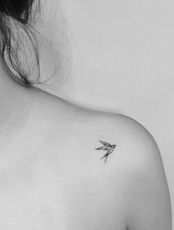 Minimalistic bird tattoo on upper shoulder, black ink line art on skin, simple and elegant design, gray background.