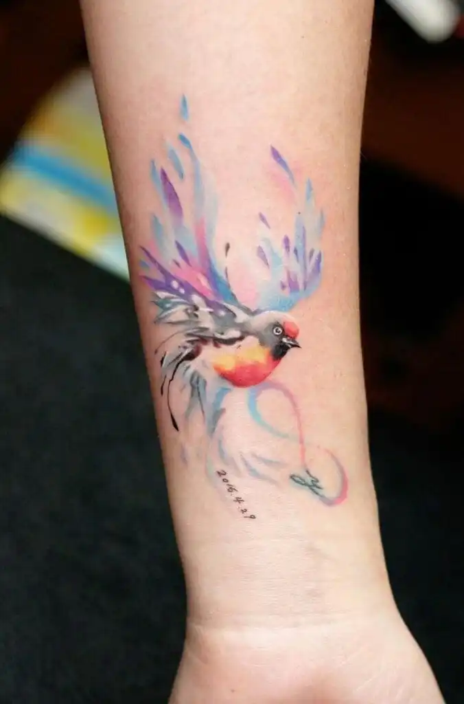 Colorful bird tattoo on forearm, featuring vibrant wings and dynamic design, symbolizing freedom and creativity in