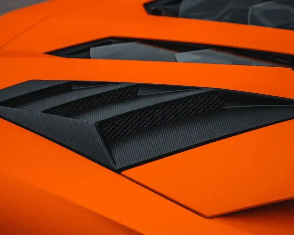 Close-up of an orange sports car vent with carbon fiber detailing, highlighting sleek design and performance features.
