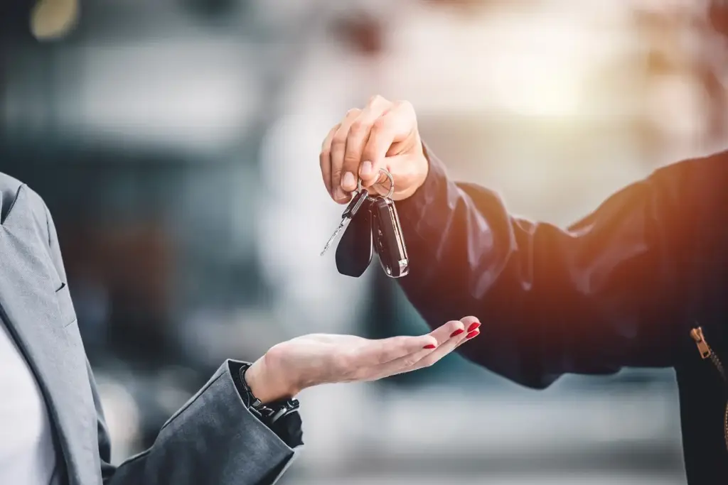 image-closeup-male-hand-giving-a-car-key Close-up of a hand handing over car keys to another, symbolizing a car purchase or rental transaction in a dealership setting. | Sky Rye Design Close-up of a hand handing over car keys to another, symbolizing a car purchase or rental transaction in a dealership setting.