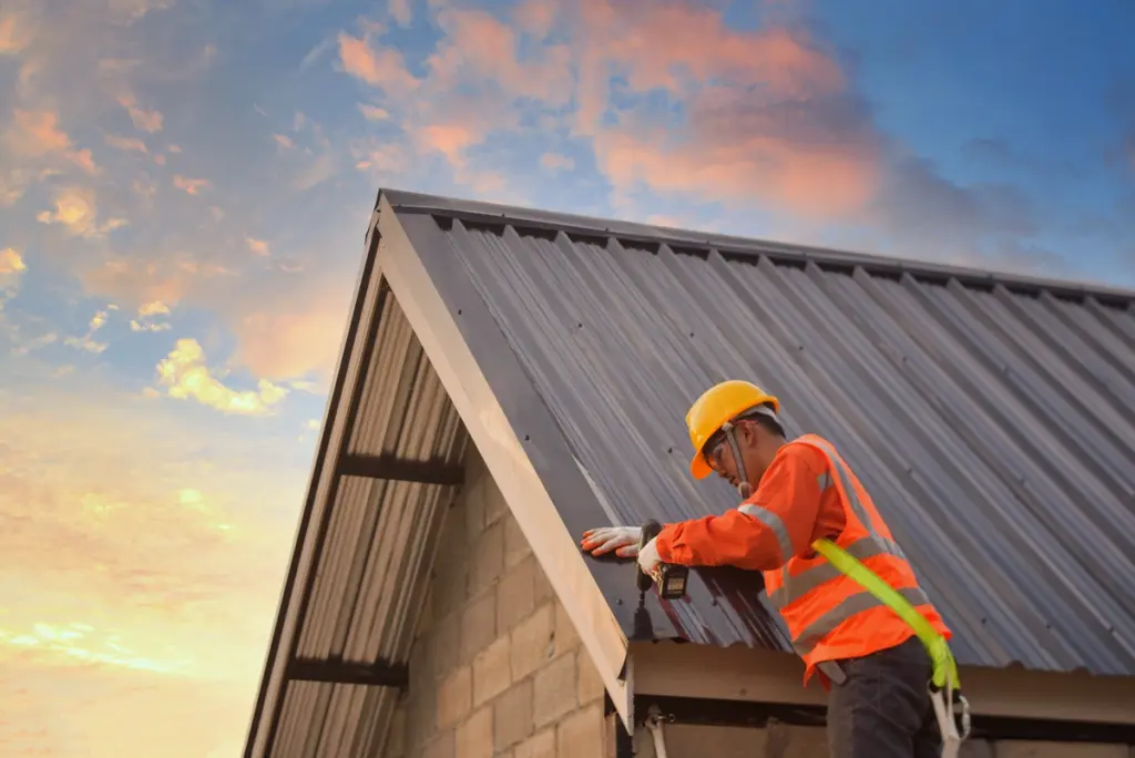 Construction worker installing metal roofing on a house at sunset, wearing safety gear for protection and precision.