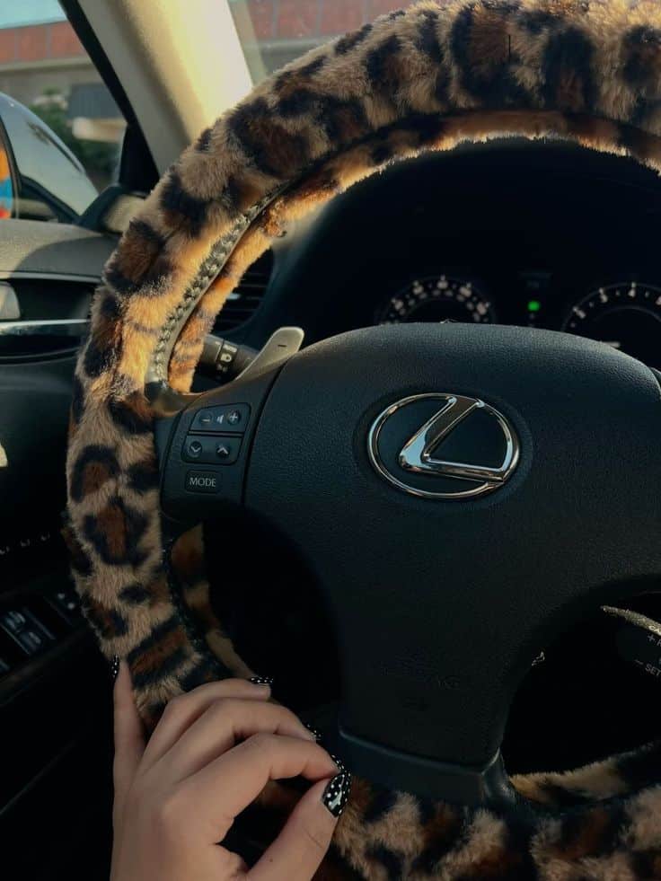 Luxurious car interior with a leopard print steering wheel cover, showing a hand with stylish nails, driving experience.