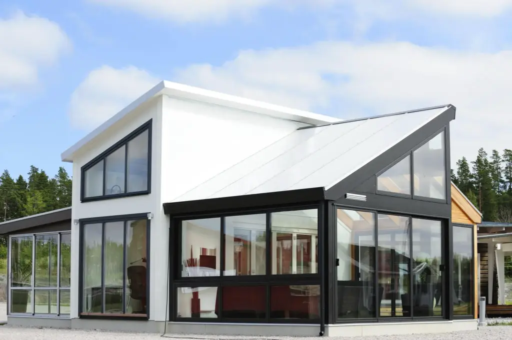 Modern house exterior with large glass windows, black and white angular design, under a blue sky with trees in the background.