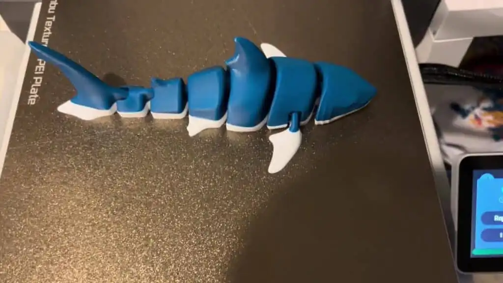 3D printed blue and white shark model on textured surface, showcasing intricate segmented design.