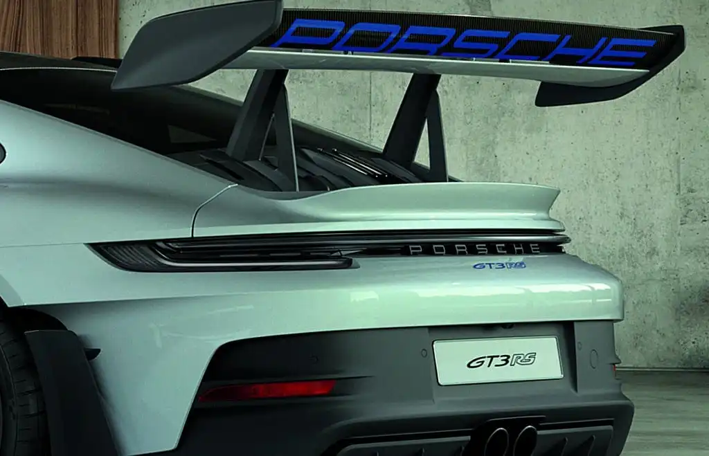 Close-up of a sleek gray Porsche GT3 RS rear with a prominent spoiler and modern design against a concrete background.