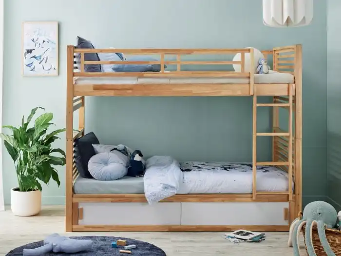 Wooden bunk bed setup in a kids' room with plush toys and pastel decor, featuring blue bedding and a plant for a cozy