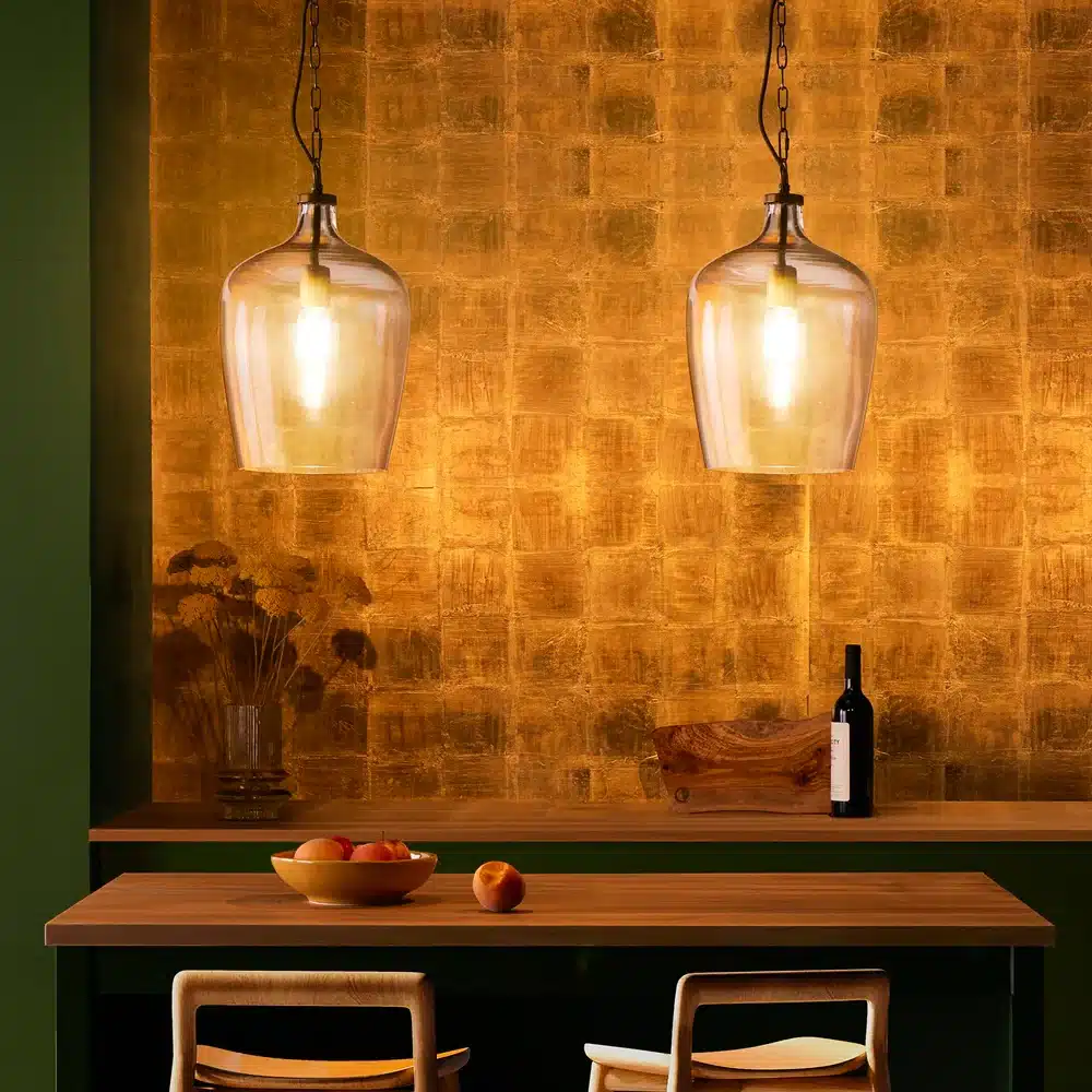 rumeli_lit Warm dining area with pendant lights, wooden table, fruit bowl, and wine bottle against a textured gold wall background. Cozy and inviting ambiance. | Sky Rye Design Warm dining area with pendant lights, wooden table, fruit bowl, and wine bottle against a textured gold wall background. Cozy and inviting ambiance.