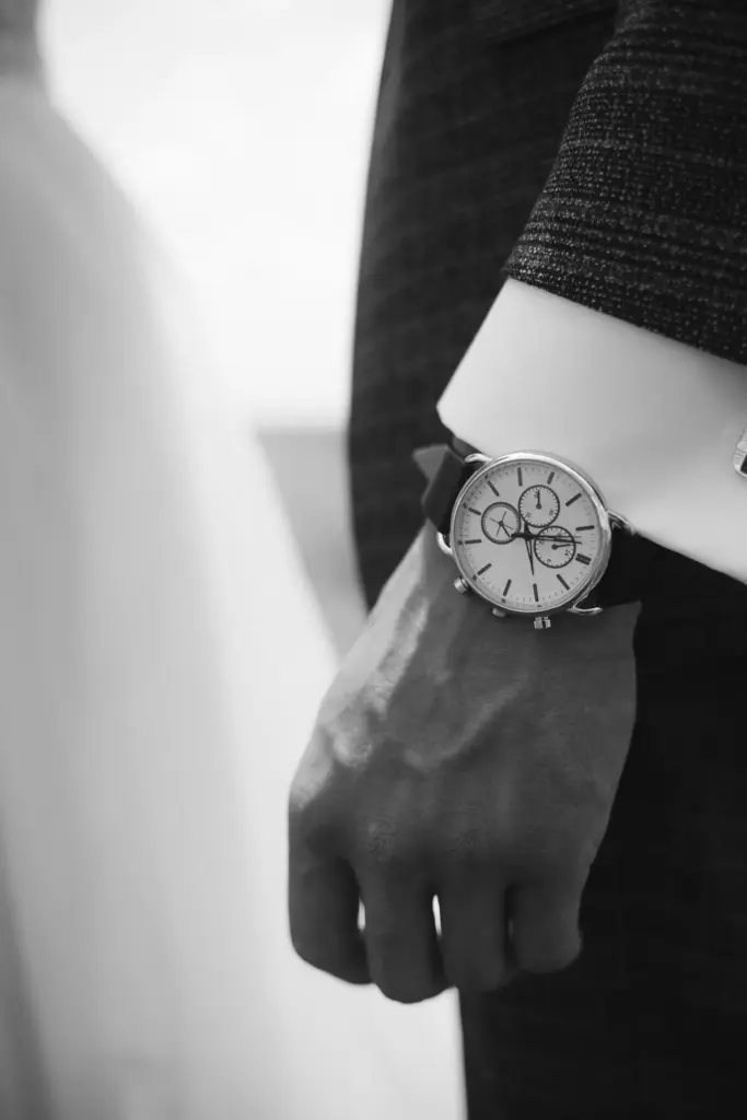 Black and white photo of a person wearing a stylish wristwatch with a leather strap, complementing a formal suit.