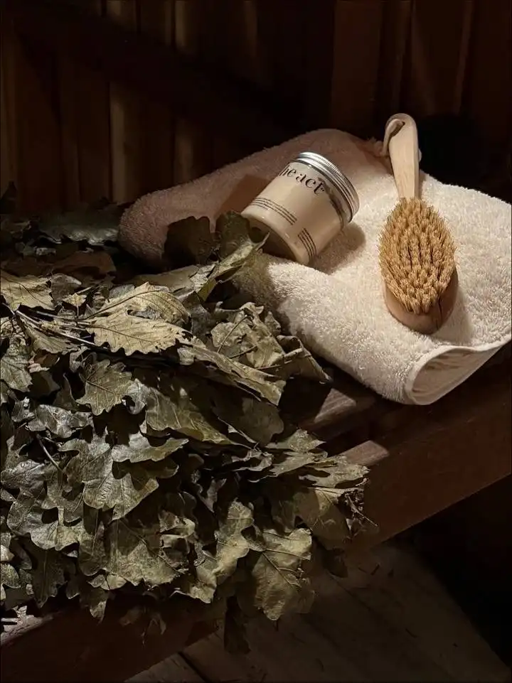 Spa essentials: bath brush, towel, jar, and oak leaves on a wooden bench. Perfect for a relaxing sauna or wellness routine.