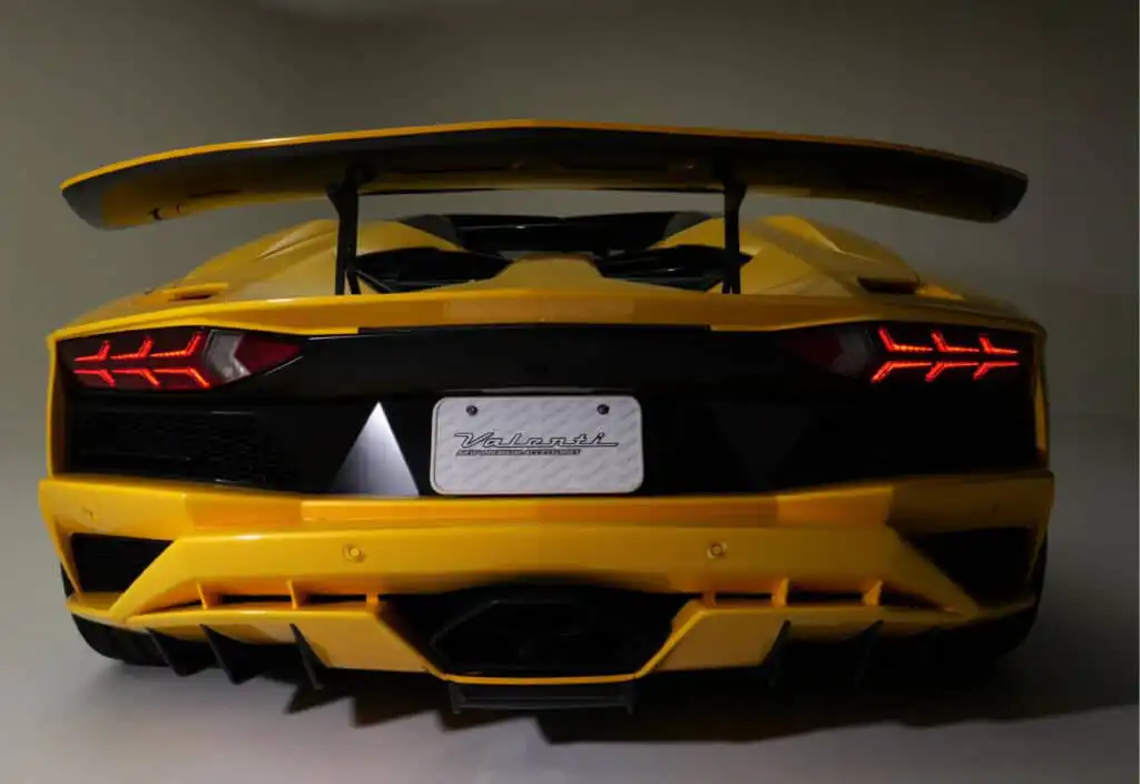Yellow sports car rear view with spoiler and illuminated tail lights in studio setting. Sleek design highlights performance