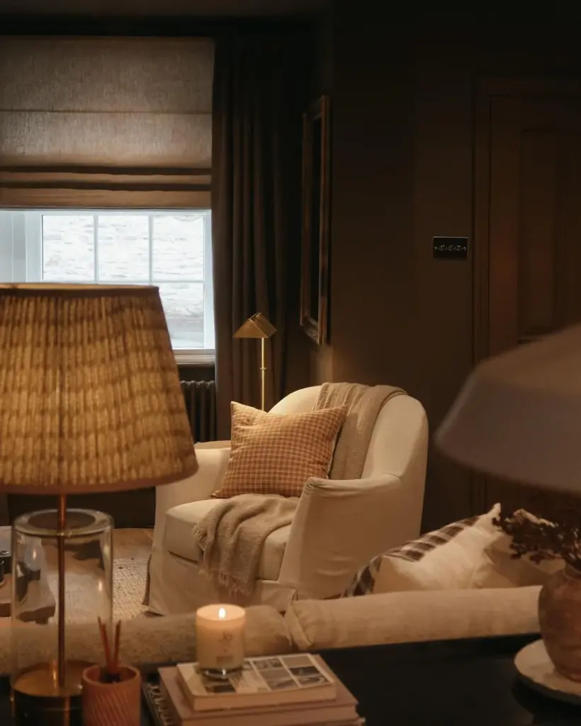 toby_sitting_room_83355922-a570-4cd8-b920-88c1d6f70b5e Cozy living room with a white armchair, soft plaid blanket, and warm lighting; candles and books add a homely touch to the decor. | Sky Rye Design Cozy living room with a white armchair, soft plaid blanket, and warm lighting; candles and books add a homely touch to the decor.