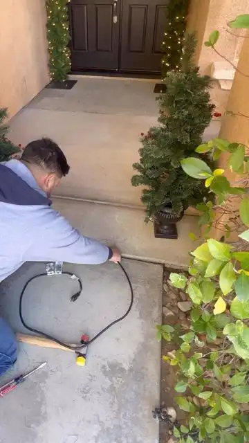 Person using a snow blower to clear a driveway in front of a snow-covered house. Winter weather, snow removal, and outdoor