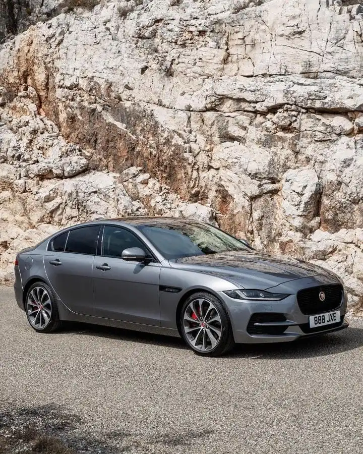 Silver luxury sedan parked in front of a rocky cliff, showcasing sleek design and elegance in a natural setting.