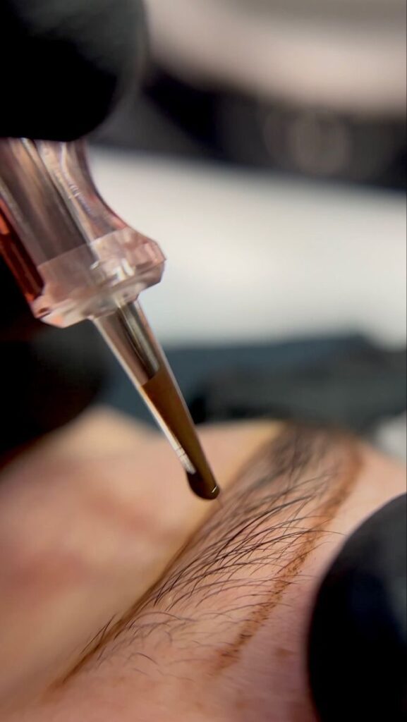 _ Close-up of a microblading needle applying ink for eyebrow enhancement, demonstrating precision in beauty treatment. | Sky Rye Design Close-up of a microblading needle applying ink for eyebrow enhancement, demonstrating precision in beauty treatment.