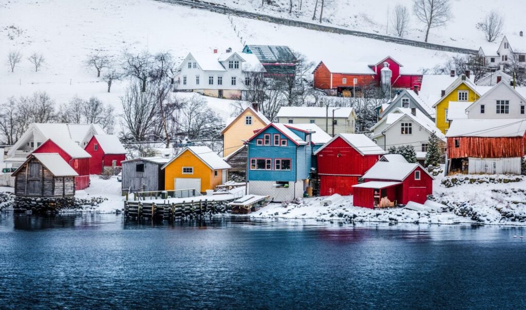 Colorful houses in a snowy Scandinavian village by the water, showcasing vibrant red, blue, and yellow hues against a winter landscape.