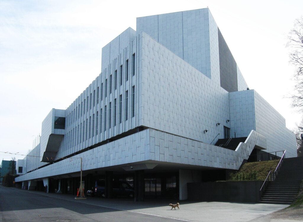 Modern white building with geometric design, featuring large windows and exterior stairs, under a clear sky.