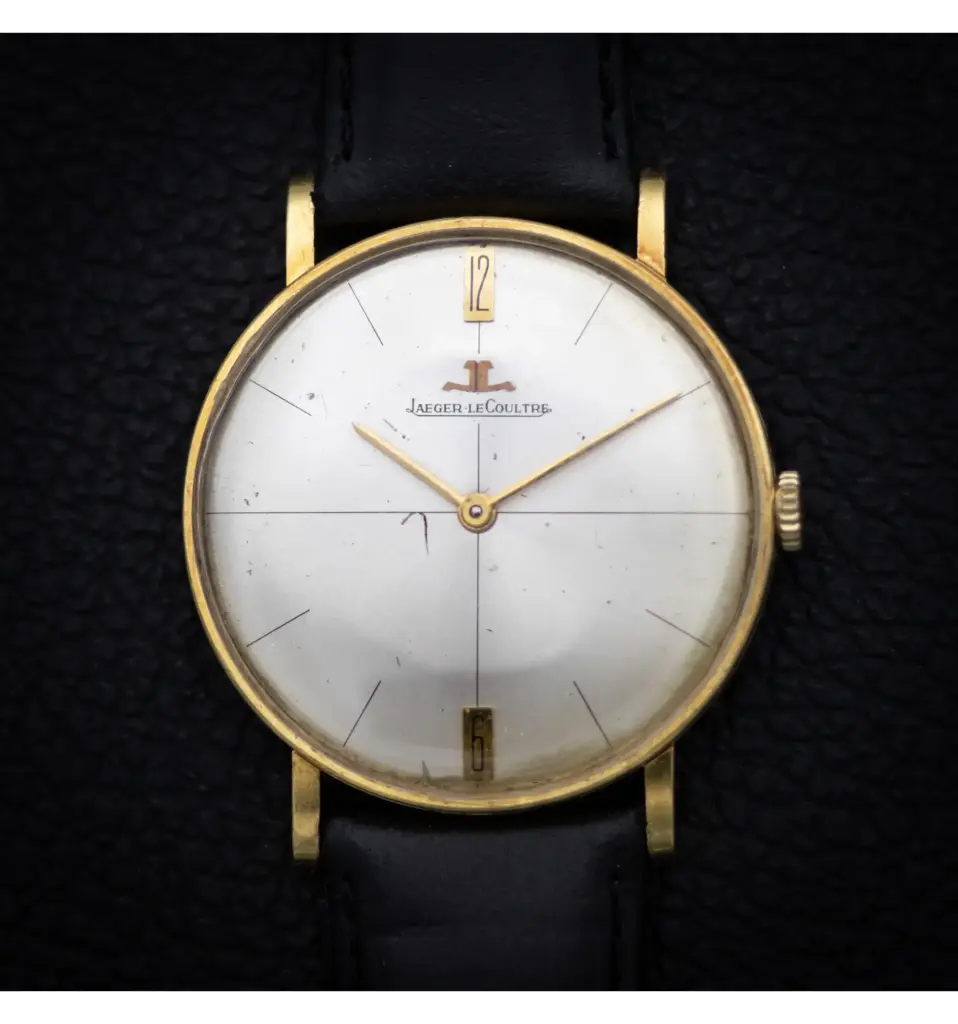 Vintage Jaeger-LeCoultre watch with gold bezel and black leather strap, showcasing elegant minimalist design on a textured black background.