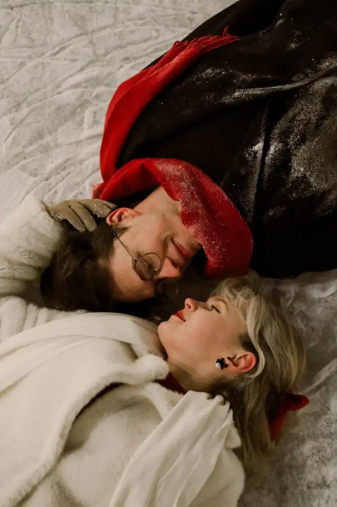 Парная фотосессия на катке _ Зимняя эстетика 1 Couple in winter coats and red scarves lying on snow, facing each other with smiles, capturing a romantic winter moment. | Sky Rye Design Couple in winter coats and red scarves lying on snow, facing each other with smiles, capturing a romantic winter moment.