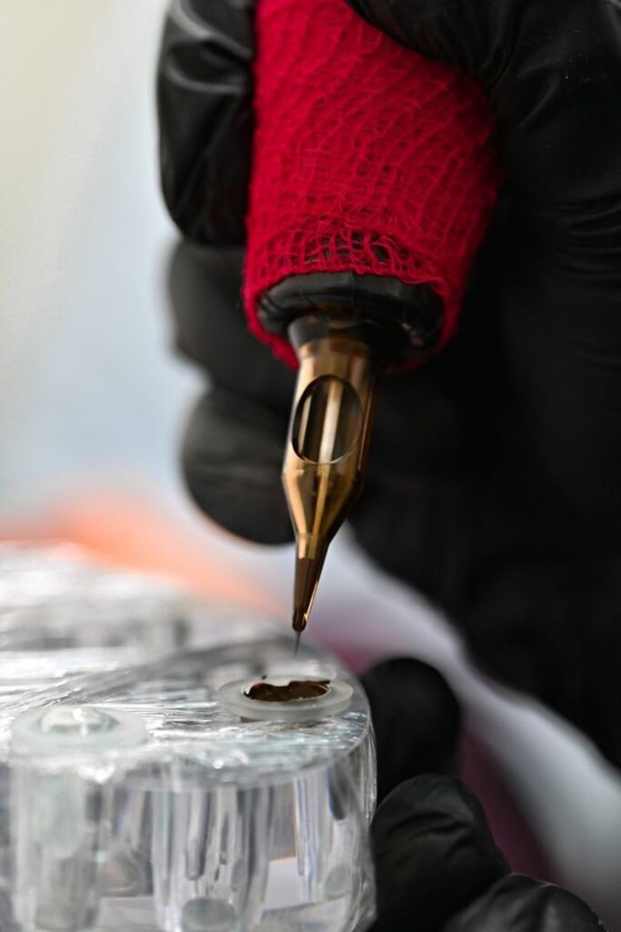 Перманент Tattoo artist with black gloves handling a red-wrapped tattoo machine, preparing ink for use. | Sky Rye Design Tattoo artist with black gloves handling a red-wrapped tattoo machine, preparing ink for use.