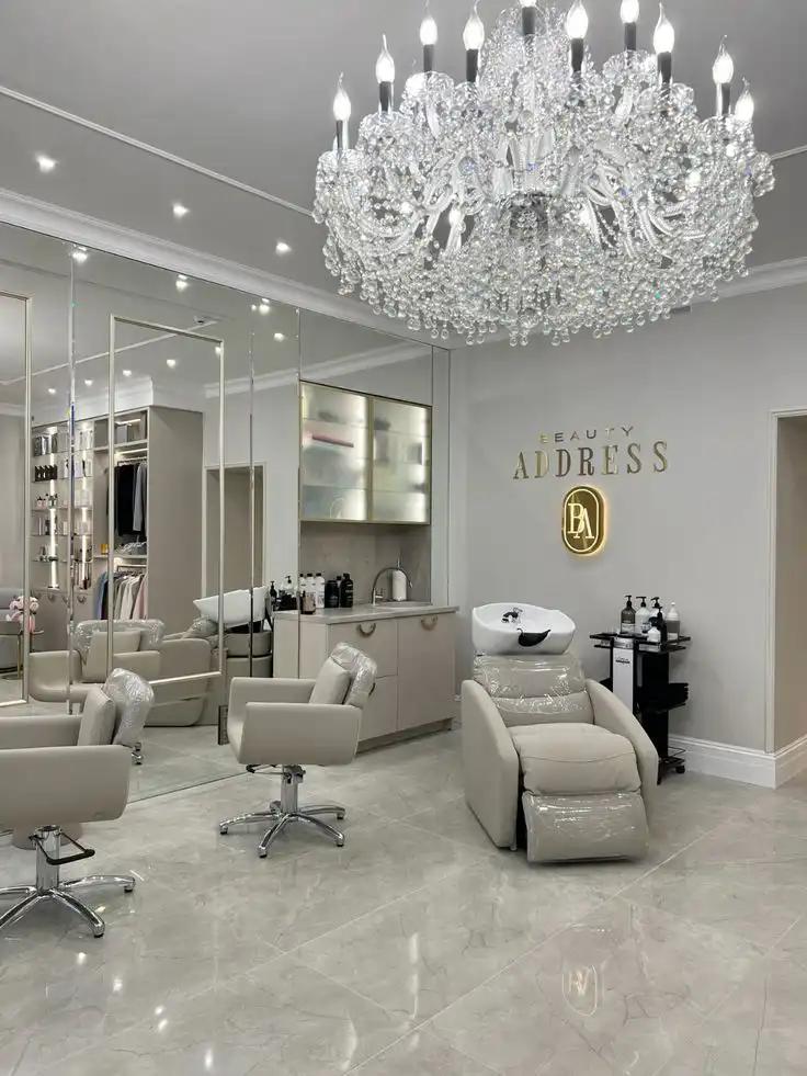 Luxurious beauty salon interior with elegant chandelier, mirrored walls, and modern furnishings for hair services.
