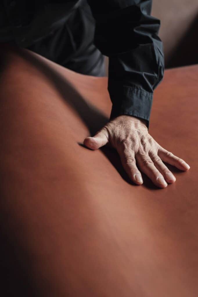 土屋鞄を生んだ哲学と美学 Hand touching smooth brown leather surface, showcasing texture and quality. Ideal for luxury leather goods, craftsmanship concepts. | Sky Rye Design Hand touching smooth brown leather surface, showcasing texture and quality. Ideal for luxury leather goods, craftsmanship concepts.
