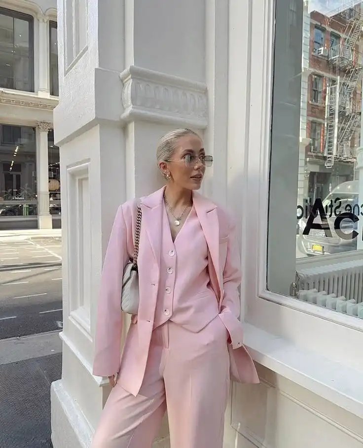Elegant woman in a pink suit poses stylishly on a city street corner, exuding confidence and modern fashion vibes.
