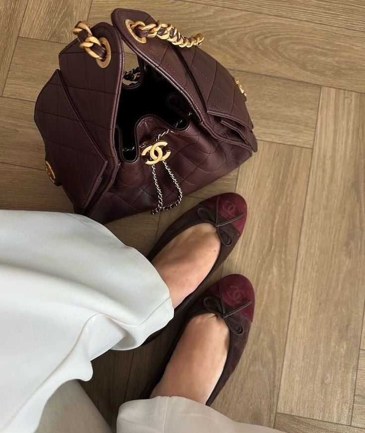 💎Vip💎_0504383115 Elegant burgundy handbag with chain detail paired with matching flats and white pants on wooden flooring. | Sky Rye Design Elegant burgundy handbag with chain detail paired with matching flats and white pants on wooden flooring.