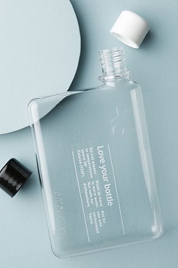 Clear flat reusable water bottle labeled Love your bottle with open white cap and black cap on pale blue minimalist background