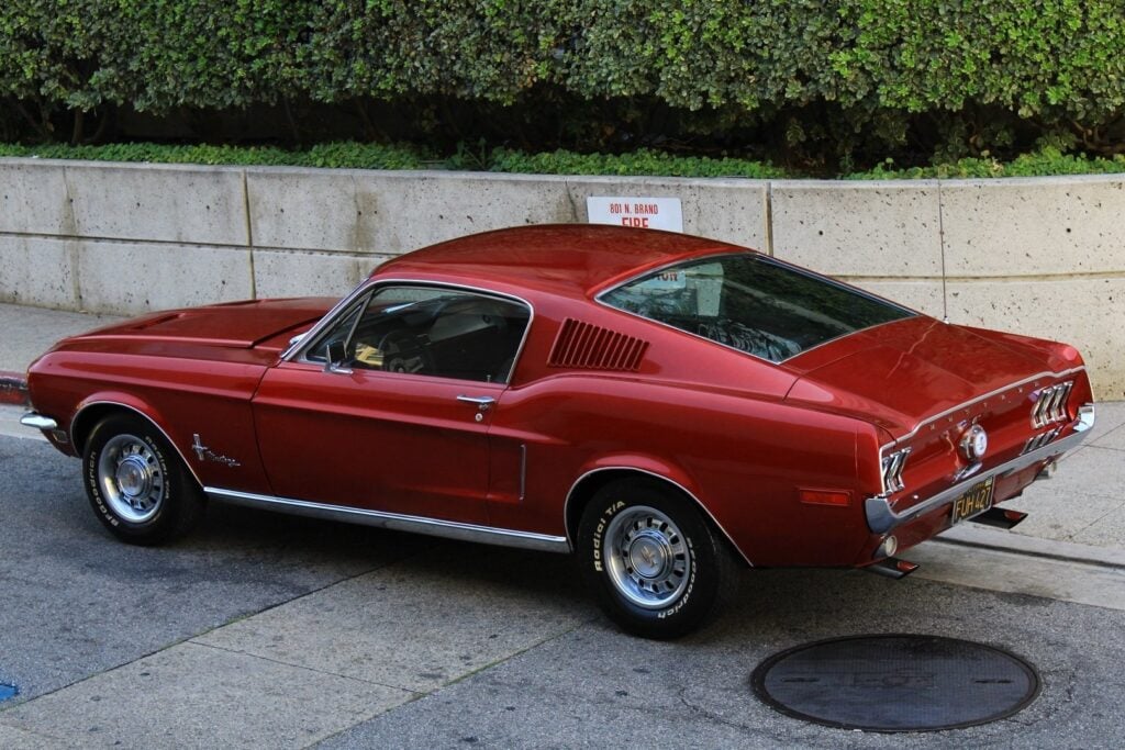 Classic red Ford Mustang fastback muscle car parked on urban street, three-quarter rear view with chrome trim and polished wheels