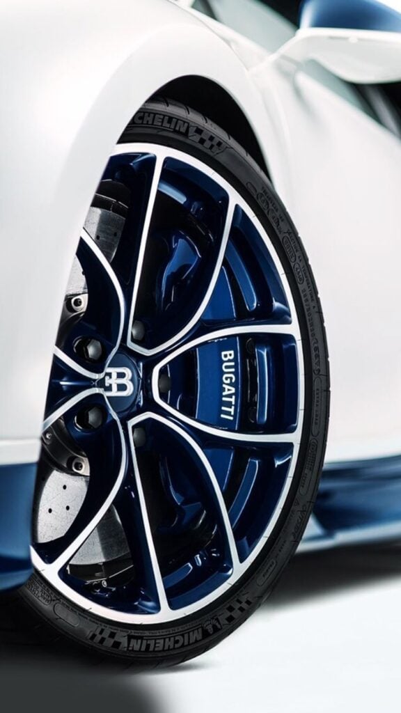 Close-up of blue Bugatti alloy wheel with Michelin tire on white luxury sports car, showing rim, brake disc, and branding