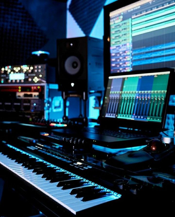 Music production studio with illuminated MIDI keyboard, laptop running DAW mixer, studio monitors and audio gear in blue ambient lighting