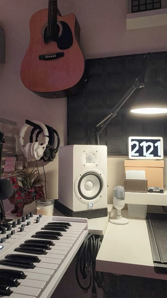 Home music studio setup: acoustic guitar, MIDI keyboard, studio monitor, headphones, microphone, desk lamp and digital clock