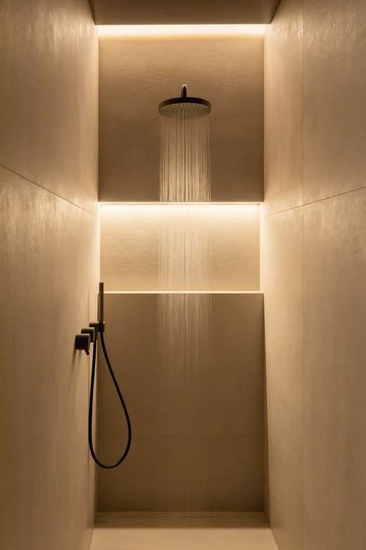 Luxury minimalist walk-in shower with overhead rain showerhead, hand shower, warm recessed LED lighting and smooth neutral-toned tiles